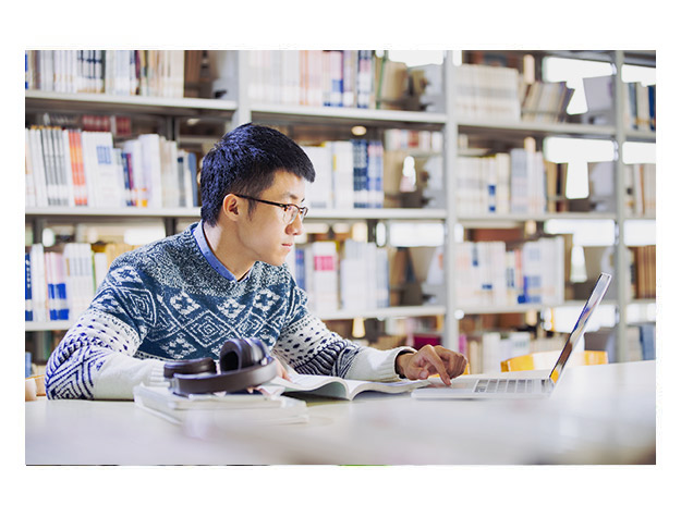 年轻男子在图书馆用笔记本电脑学习